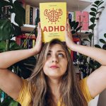na zdjęciu znajduje się kobieta trzymająca nad głową książkę w żółtej okładce ADHD. Mózg łowcy i inne supermoce Kristin Leer
