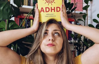 na zdjęciu znajduje się kobieta trzymająca nad głową książkę w żółtej okładce ADHD. Mózg łowcy i inne supermoce Kristin Leer